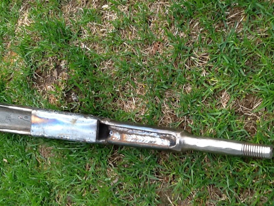 Fabricated steel link with threaded end welded into slotted square tube, lying in grass