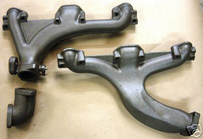 1978 Ford Bronco - Two exhaust manifolds and a pipe fitting are laid out on a surface, likely for a vehicle's engine.