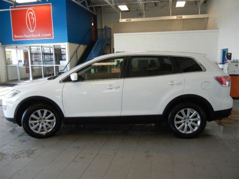 2008 Mazda CX-9 - This white SUV is parked inside a dealership with a blue and red sign visible in the background.