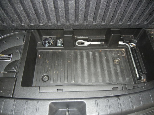 Black plastic cargo area with jack, lug wrench, and tow hook
