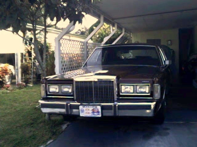 Burgundy Lincoln Town Car parked under a carport beside lattice fence