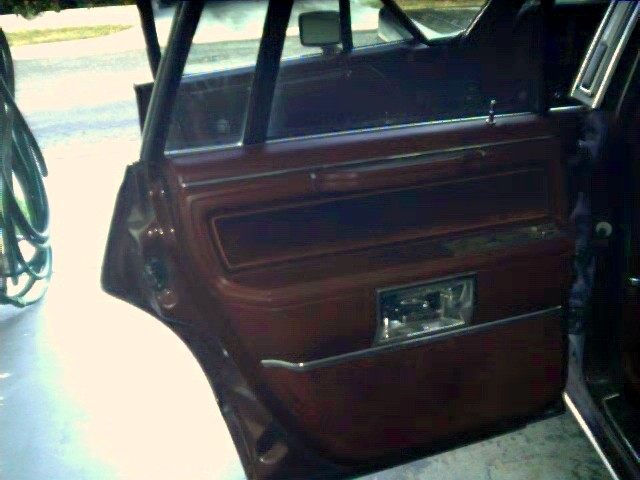 Open rear door of a sedan showing burgundy interior panel and armrest