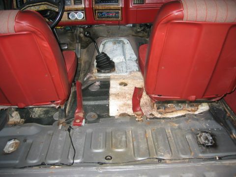 1986 Ford Bronco - Interior view of a Ford Bronco with the rear cargo area stripped to bare metal floor, showing the manual transmission shifter with black ru…