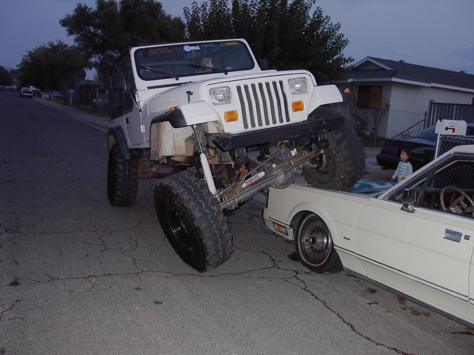 White lifted Jeep Wrangler YJ climbing onto the hood of a white coupe at dusk