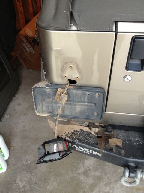 2005 Jeep Wrangler - The rear bumper of a gold Jeep Wrangler shows damage with a detached taillight and license plate bracket.