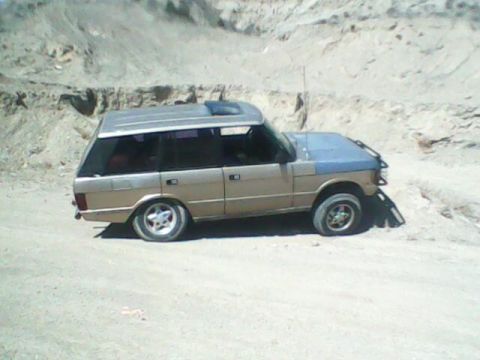 1991 Land Rover Range Rover - A tan and blue 1991 Land Rover Range Rover is parked on a dirt road with a rocky hillside in the background.