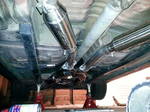 1995 Ford Mustang - Custom exhaust system installation, Magnaflow mufflers and an X-pipe, with the vehicle raised on jack stands.