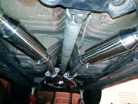 1995 Ford Mustang - The underside of a vehicle displays a custom dual exhaust system with shiny mufflers and a central driveshaft.