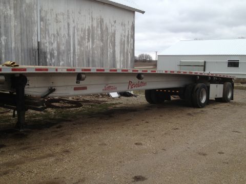 2003 Peterbilt 379 - A flatbed trailer is parked on a dirt lot in front of a weathered barn.
