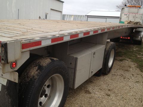 2003 Peterbilt 379 - A flatbed trailer is seen from the side, red reflectors along its edge and metal toolboxes mounted underneath.