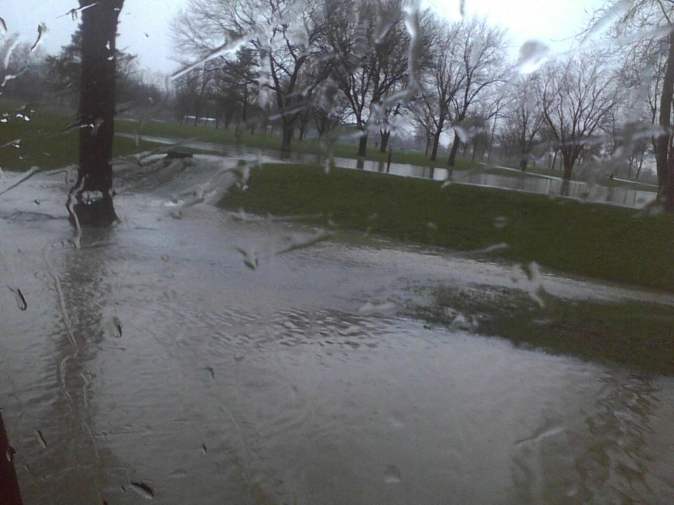 Flooded park with trees and grass, viewed through a wet window