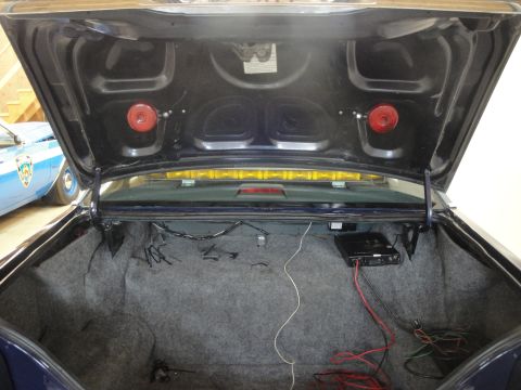 1991 Ford LTD Crown Victoria - Trunk interior of a 1991 Ford Crown Victoria LTD, showing wiring and an amplifier. A police car is partially visible.