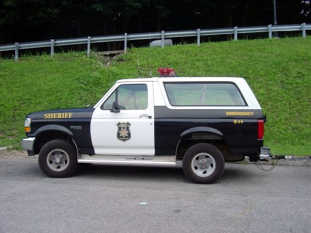 Side view of a 1994 Ford Bronco police vehicle with "SHERIFF" on the fender and "EMERGENCY 9-1-1" on the rear quarter panel