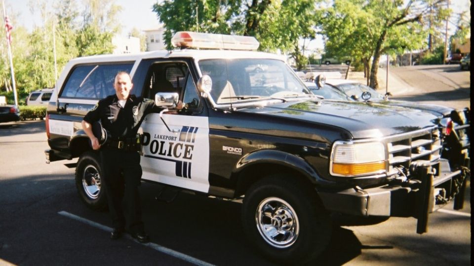 Black and white Ford Bronco police SUV with "LAKEPORT POLICE" text, parked on asphalt with a uniformed officer standing beside it