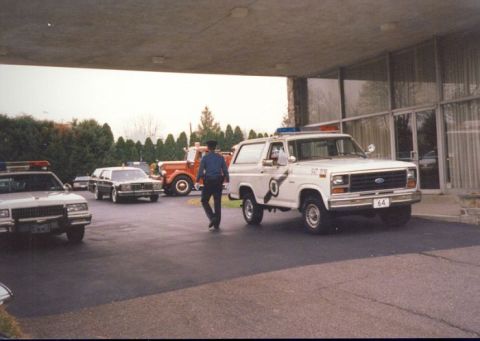 1994 Ford Bronco - A 1980s Ford Bronco, likely used by emergency services, is parked outside a building with other vehicles.