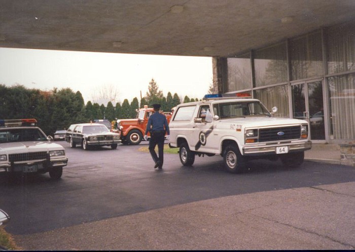 White Ford Bronco with police light bar, parked next to a police car and a fire truck