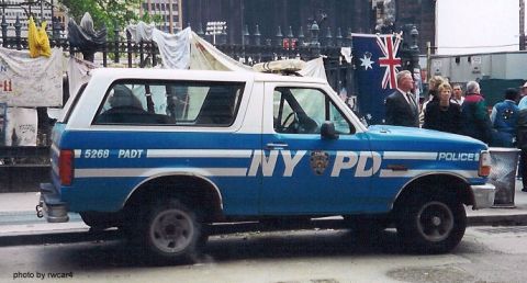 1994 Ford Bronco - A blue and white NYPD Bronco is parked on the street with people in the background.