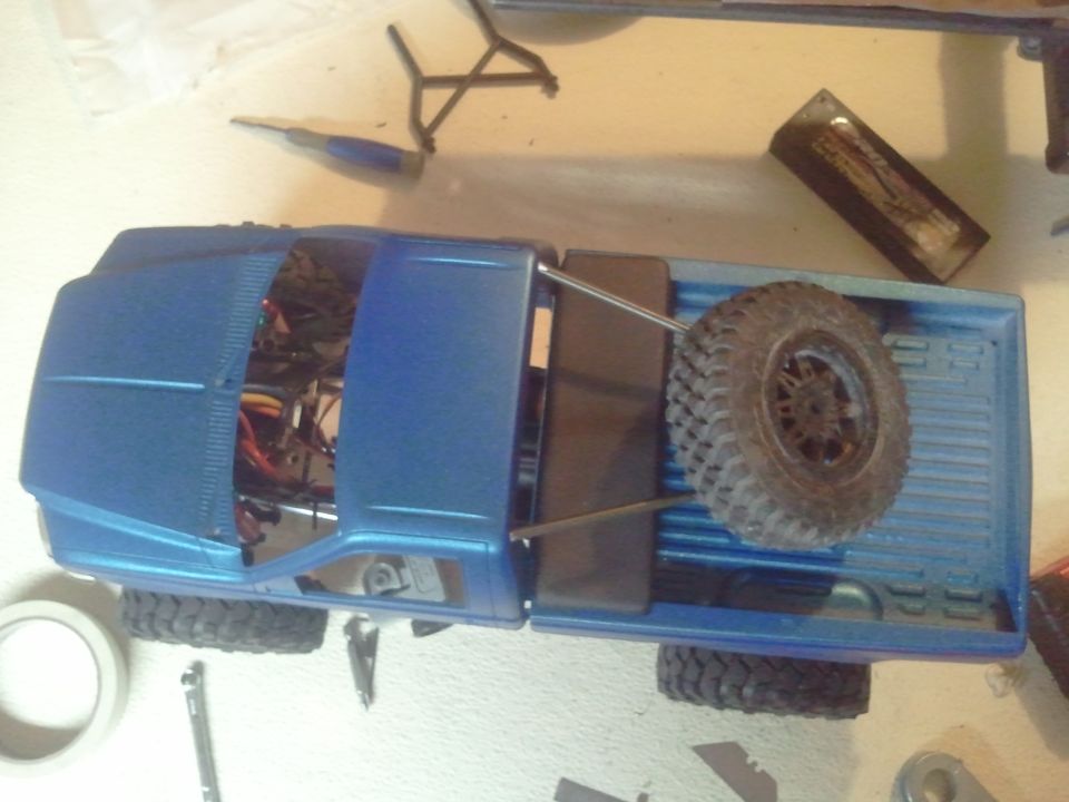 Blue RC truck bed with spare tire mounted inside. Tools and tape are on the surface