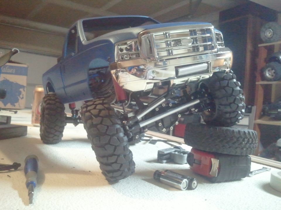 Blue RC truck model with chrome grille and large off-road tires, viewed from a 3/4 front angle