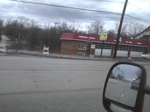 2003 Ford Crown Victoria - An auto shop with 'EMISSION CONTROL' and 'AUTO REPAIR' signs is visible next to a flooded area, with traffic cones and barriers present.