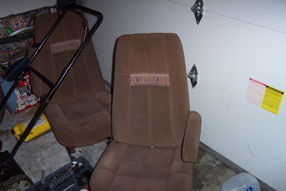 Brown cloth bucket seats with tree-pattern stripe removed and sitting in a garage