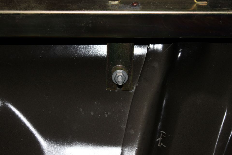 Close-up of a metal bracket with a bolt and washer attached to a dark surface inside a vehicle