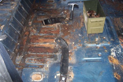1980 Ford Bronco - Bare blue-painted cargo floor of a truck with carpet and seats removed, showing surface rust along the ribbed stampings, exposed bolt holes…