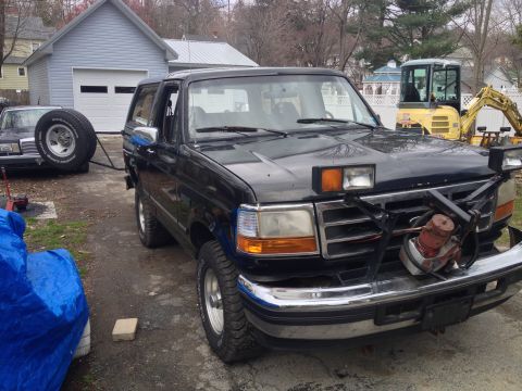 1996 Ford Bronco - Black Ford Bronco with a plow mount and auxiliary lights is parked outside a garage.