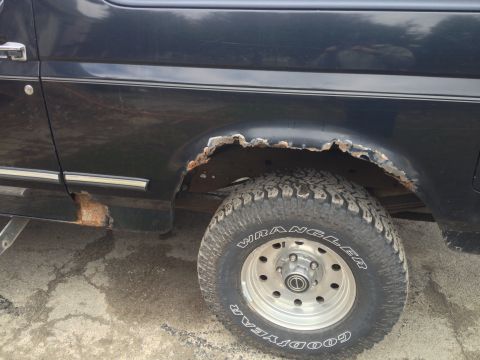1996 Ford Bronco - This dark blue Ford Bronco shows extensive rust around the rear wheel well and lower body panel.