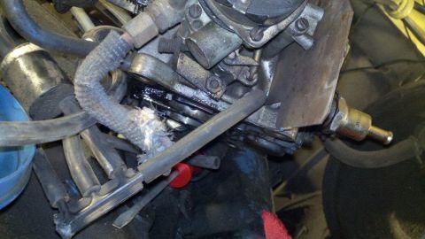 1978 Ford Bronco - Close-up view of a vehicle's engine carburetor and associated fuel lines, showing wear and tear on a hose.