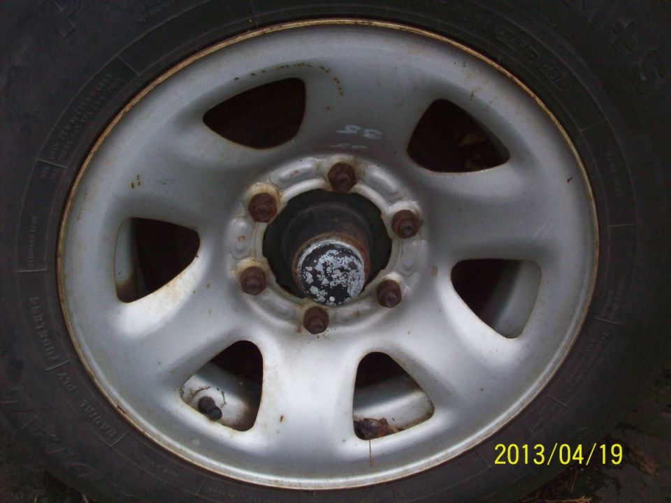 Close-up of a silver wheel with five lug nuts and a black center cap. Tire is visible around the rim
