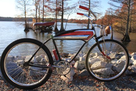 1994 Ford Bronco - A vintage bicycle with red handlebars and seat sits on a rocky shore with a lake and trees in the background.