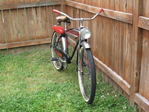 1994 Ford Bronco - A vintage bicycle with a red seat and handlebars rests against a weathered wooden fence in a grassy yard.