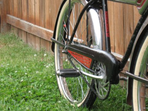 1994 Ford Bronco - Detail of a vintage bicycle's chain guard and rear wheel assembly against a wooden fence.