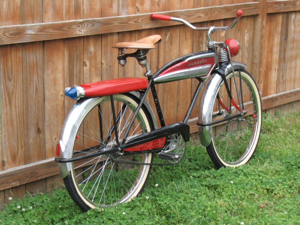 Red and chrome bicycle with 'J.C. Higgins' on the frame, leaning against a wooden fence