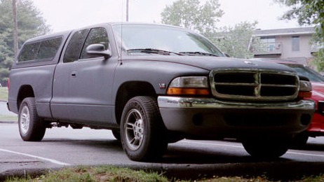 1991 Ford LTD Crown Victoria - A dark gray pickup truck with a camper shell is parked outside. Another red vehicle is partially visible.
