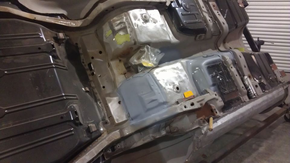Undercarriage of a vehicle undergoing repair, showing metal framing, fuel tank area, and some yellow markings
