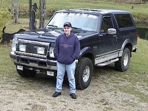 1995 Ford Bronco - A person stands in front of a dark blue 1995 Ford Bronco parked outdoors.