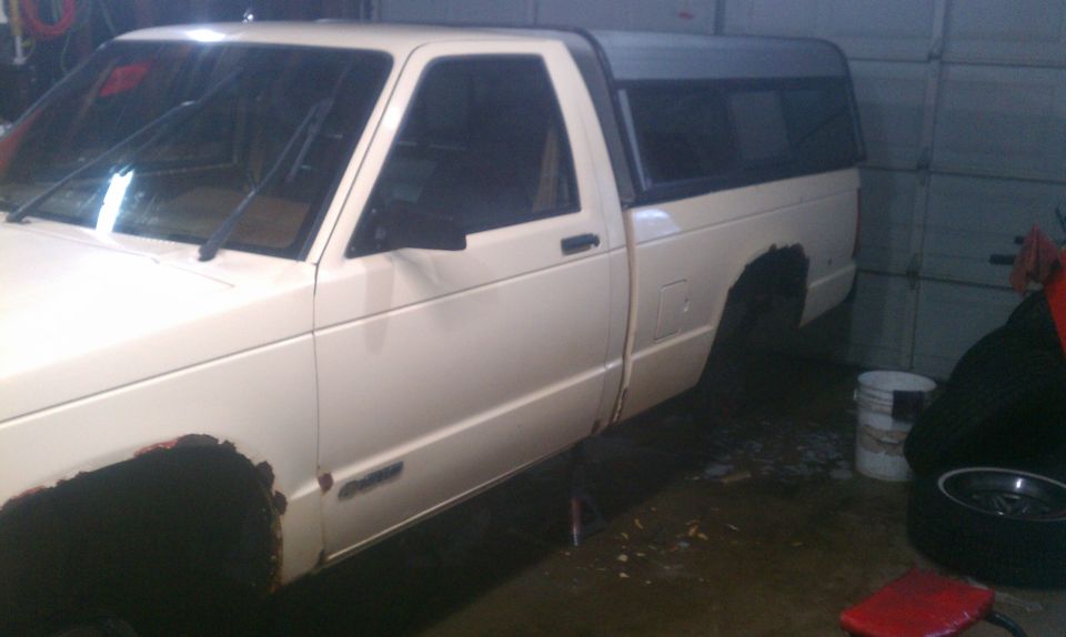 1991 Chevrolet S10 pickup truck with a black camper shell, showing rust on wheel wells