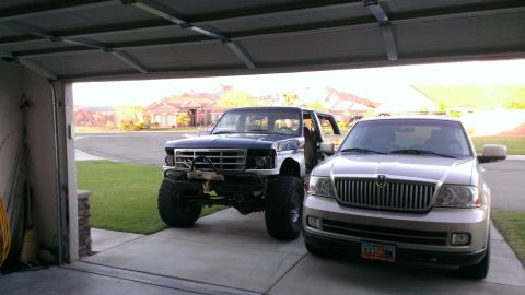 1994 Ford Bronco - A modified Ford Bronco sits in a garage next to a silver SUV, its front end showing off-road modifications.