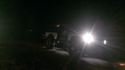 1994 Ford Bronco - A vehicle's headlights are brightly illuminated against the dark night sky, with a website logo in the corner.