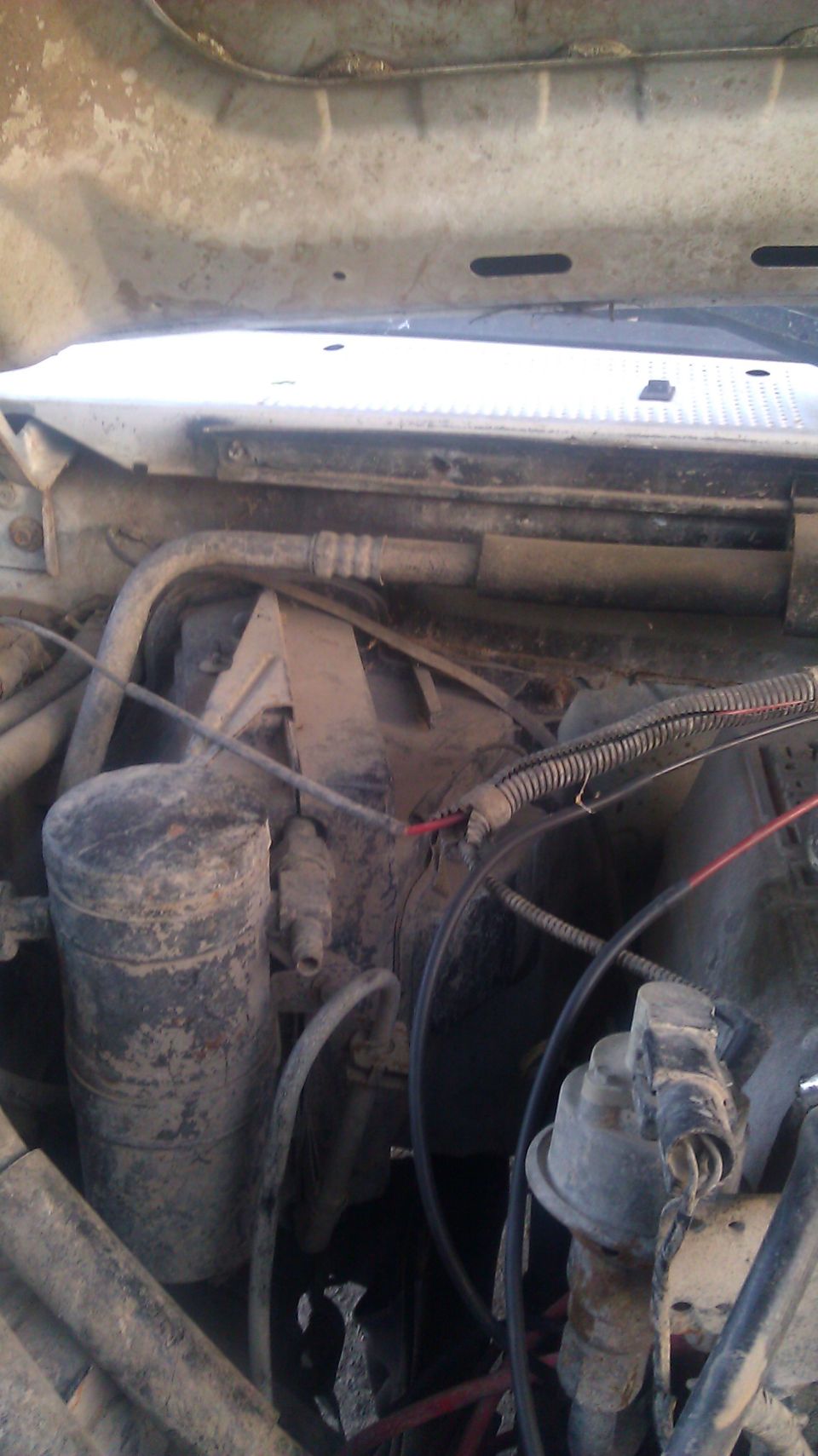 Engine bay with various hoses, wires, and a cylindrical component