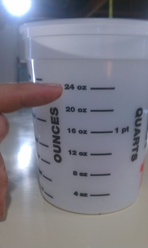 1991 Chevrolet S10 - A white plastic measuring cup displays ounce and quart measurements, with a finger indicating the 24 oz mark.