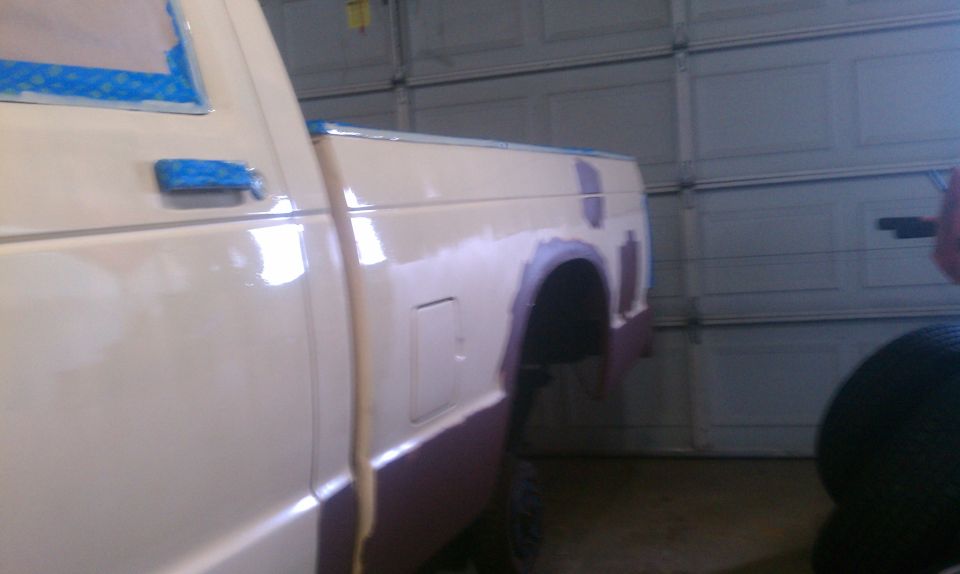 White pickup truck bed and rear quarter panel with body filler and primer, taped windows, in a garage