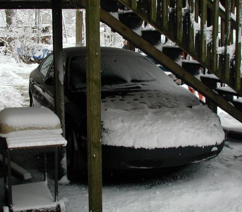 1998 Ford Taurus - A car is parked outdoors and covered in a thick layer of snow, with a wooden staircase overhead.