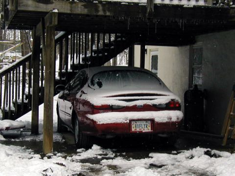 1998 Ford Taurus - A red 1998 Ford Taurus sits covered in snow under a wooden deck during winter.