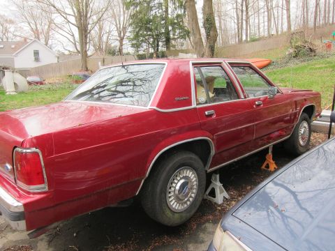 1991 Ford LTD Crown Victoria - A red 1991 Ford Crown Victoria LTD sedan is parked on jack stands in a driveway.