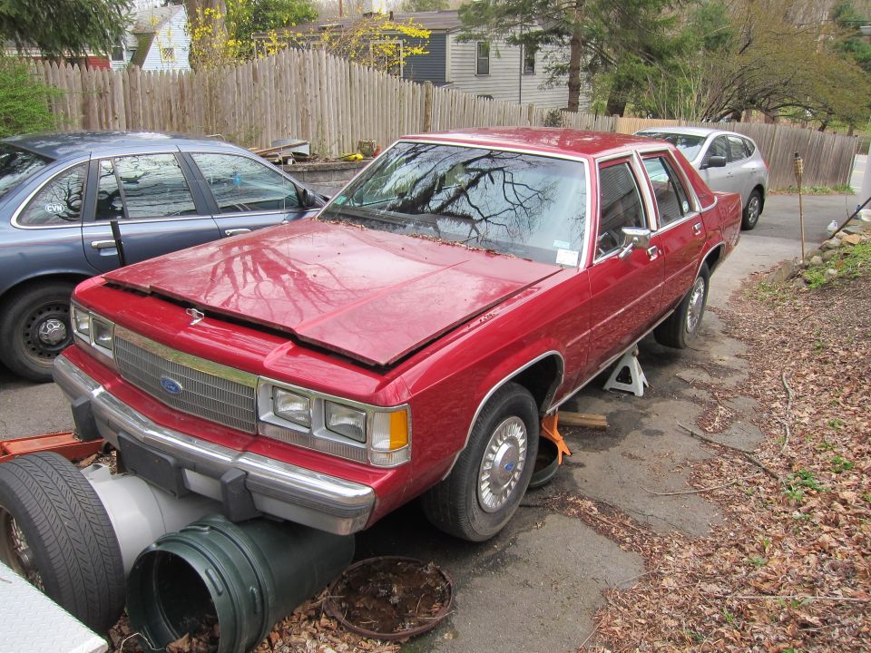 Red sedan on jack stands, hood open, with a blue sedan parked behind it