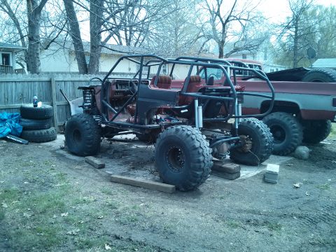 1986 Ford Bronco - A heavily modified off-road vehicle sits in a yard next to a pickup truck.