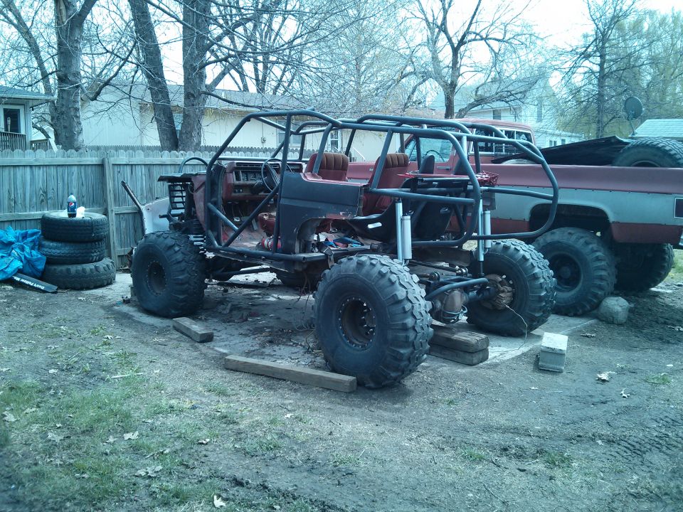 Off-road buggy with roll cage and large tires, partially disassembled, next to a red pickup truck